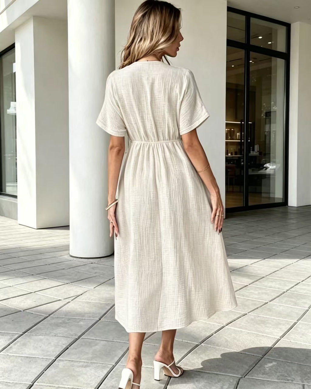 Woman wearing a beige dress walking on a tiled patio.
