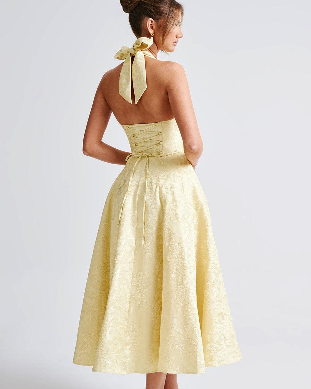Woman wearing a yellow dress with a bow detail on a white background