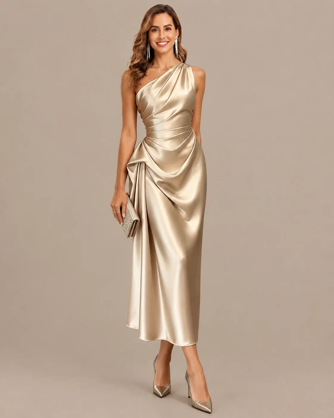 A woman modeling a one-shoulder midi dress made of shiny champagne satin, paired with pointed-toe heels and holding a small metallic clutch, set against a solid warm gray studio background.