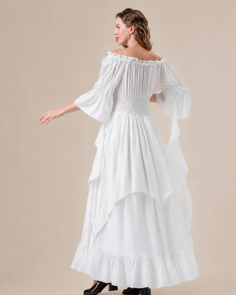 A woman modeling a white off-the-shoulder maxi dress with a smocked bodice, tiered ruffle skirt, and dramatic bell sleeves against a solid beige studio background.