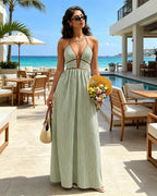 Woman in a green dress holding flowers and a bag, standing in a luxurious outdoor setting with ocean view.