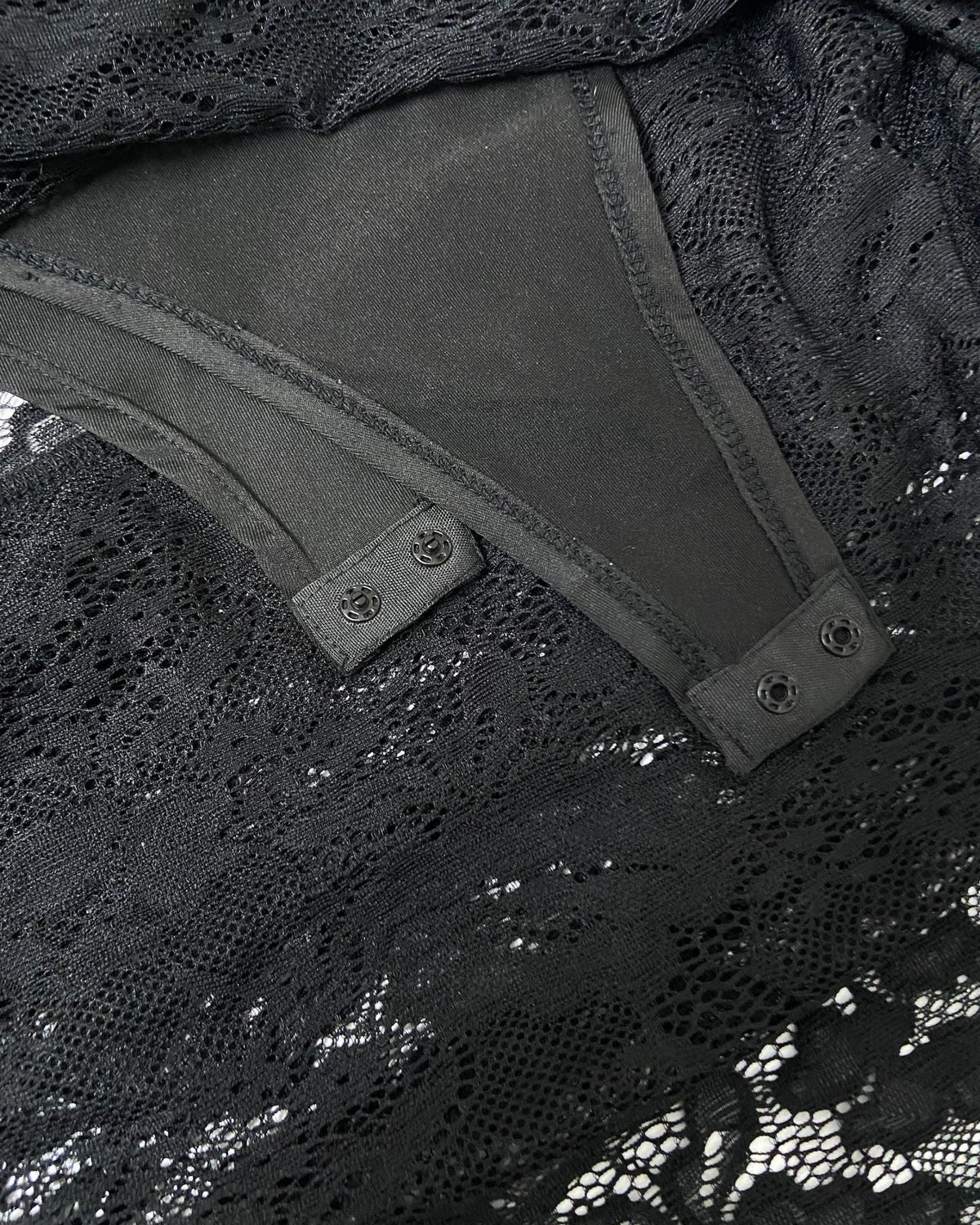 Close-up of a black lace garment with a smooth dark gray or charcoal inner panel and snap-button tabs.