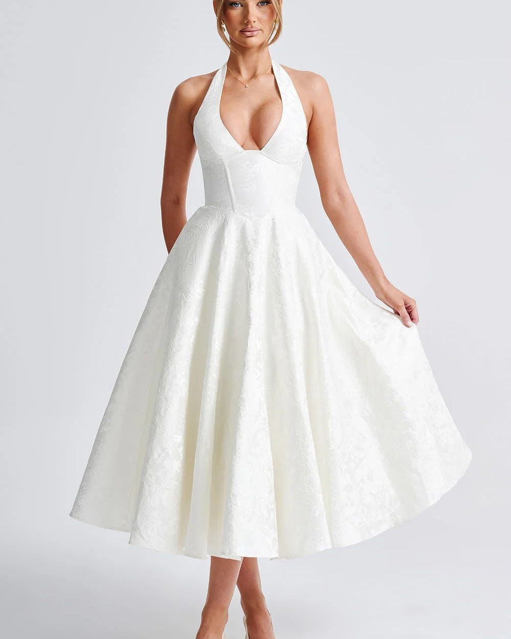Woman wearing a white halter neck dress on a plain background
