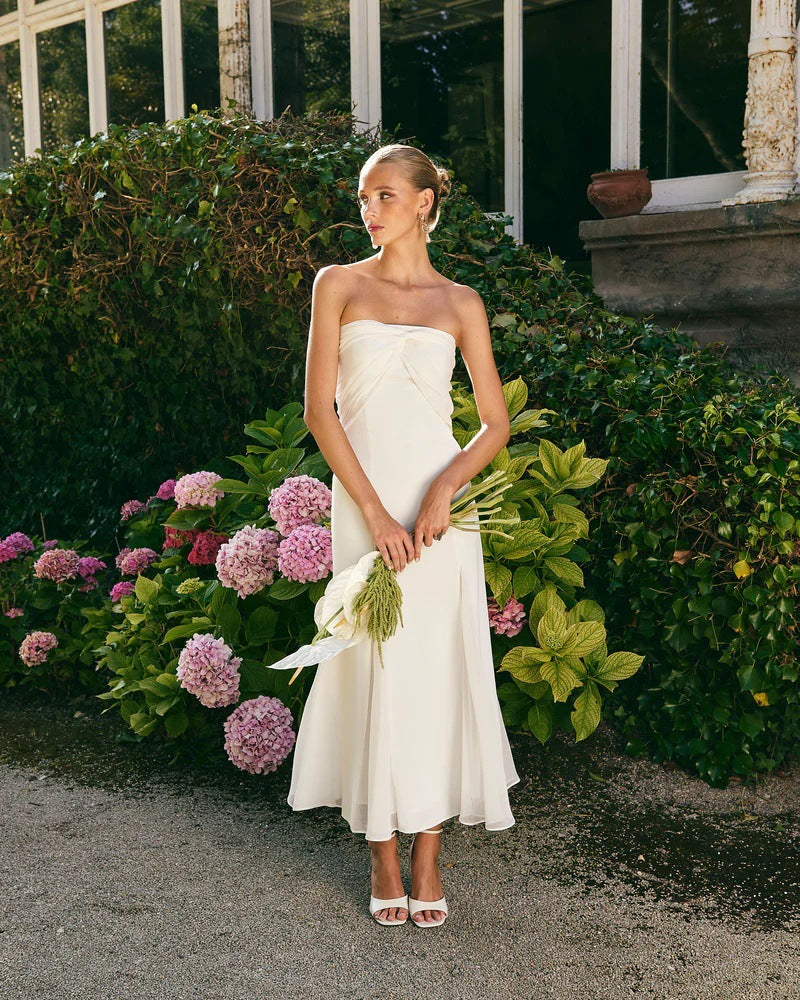 Woman in a white strapless dress holding flowers in front of greenery
