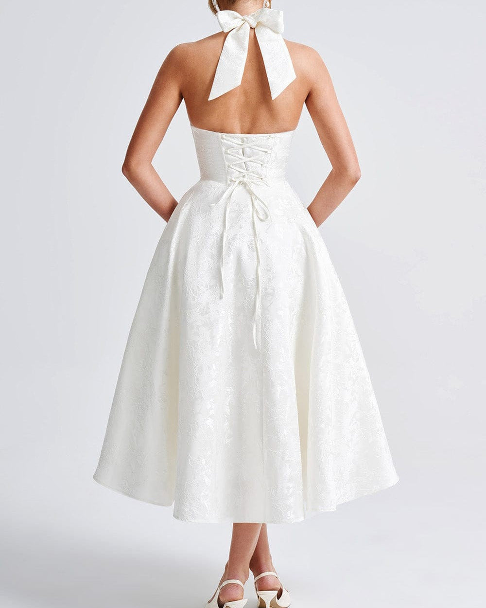 White dress with a bow detail on the back worn by a person against a plain background