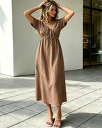 Woman wearing a brown dress standing on a tiled patio.