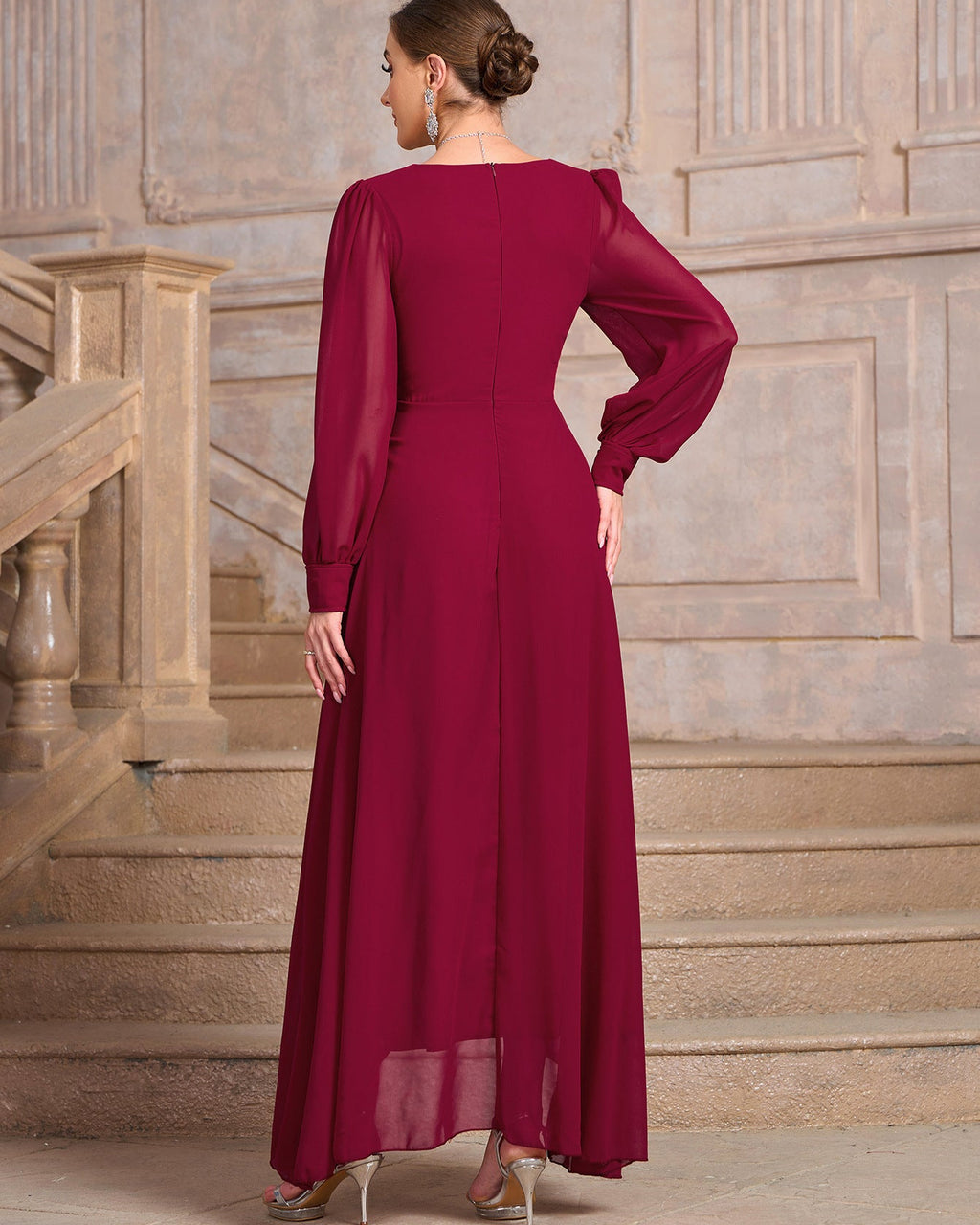 A woman wearing a long-sleeved, floor-length magenta dress, photographed from behind in front of a stone staircase.