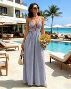 Woman in a striped dress holding flowers by a poolside with palm trees and beach chairs in the background.