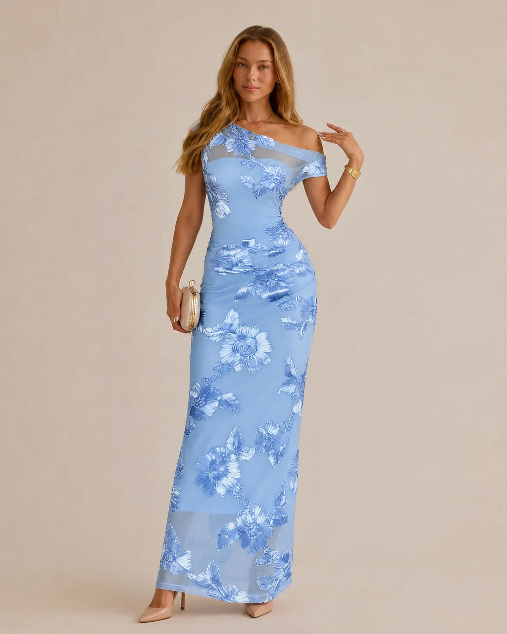 A woman models a light blue off-the-shoulder maxi dress with a white floral pattern, standing against a solid beige studio background.