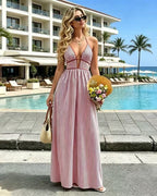 Woman in a pink striped dress standing by a pool with a hotel and ocean in the background