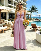 Woman in a pink and white striped dress standing by a poolside with a resort in the background.