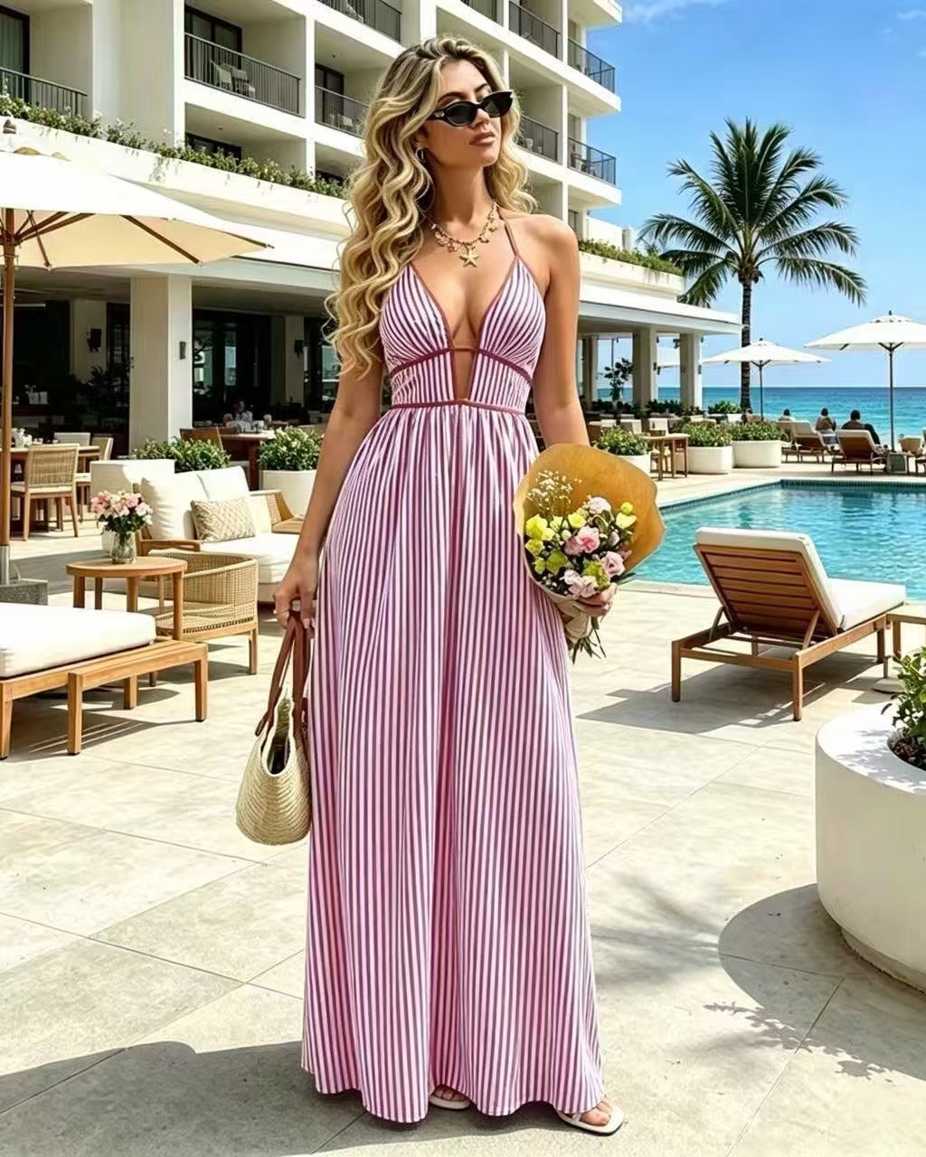Woman in a pink and white striped dress standing by a poolside with a resort in the background.