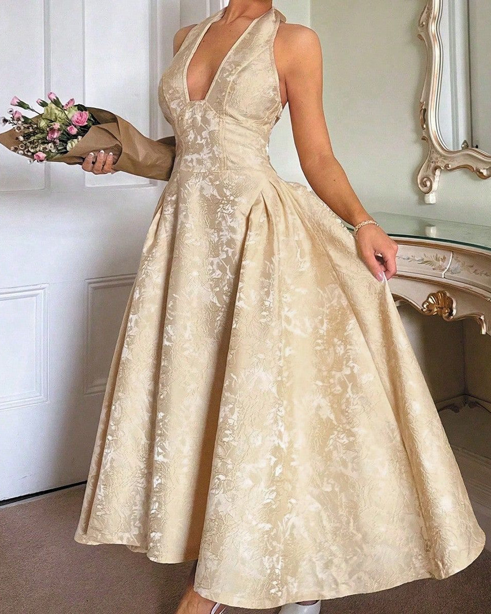 Woman in a gold evening gown holding flowers in a decorated room.