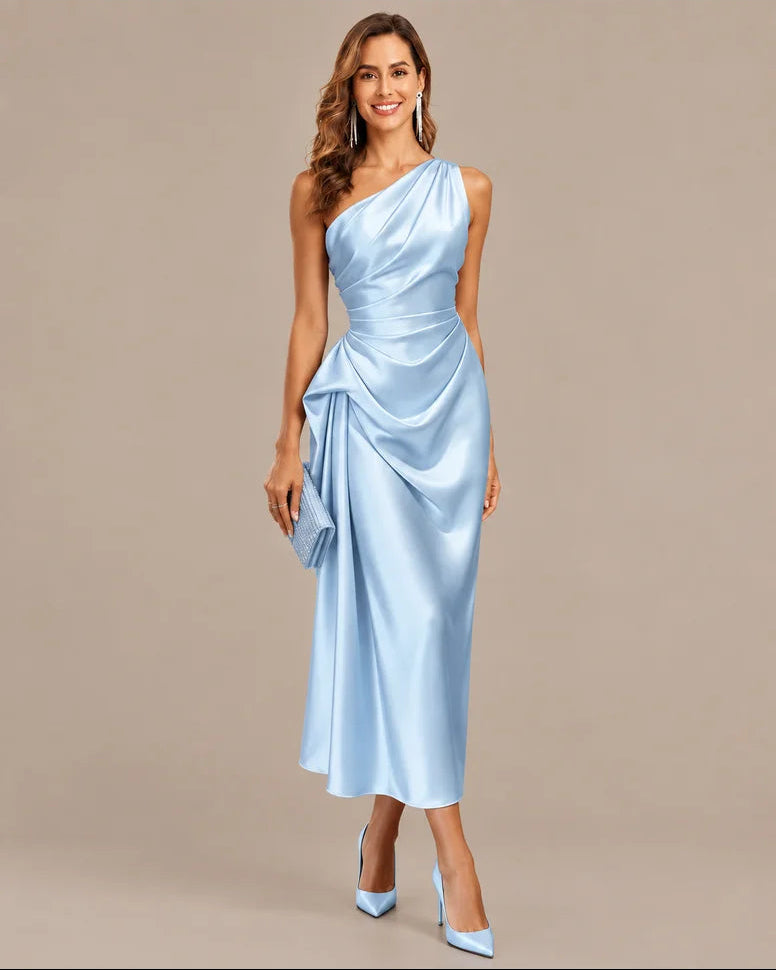 A woman modeling a light blue satin one-shoulder midi dress with draped detailing, paired with matching pointed-toe heels and a matching clutch, against a solid beige studio background.