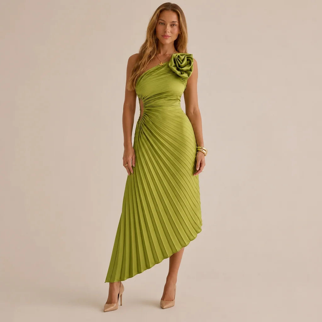 A woman models a one-shoulder midi dress in olive green with a pleated skirt and a large fabric flower detail on the shoulder, set against a plain beige studio background.